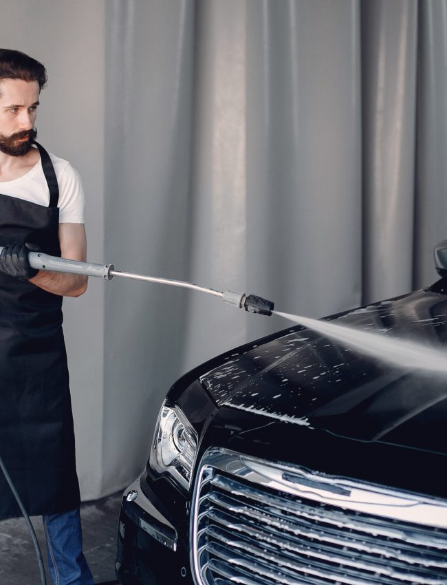 Man in a garage. Worker washing a car.